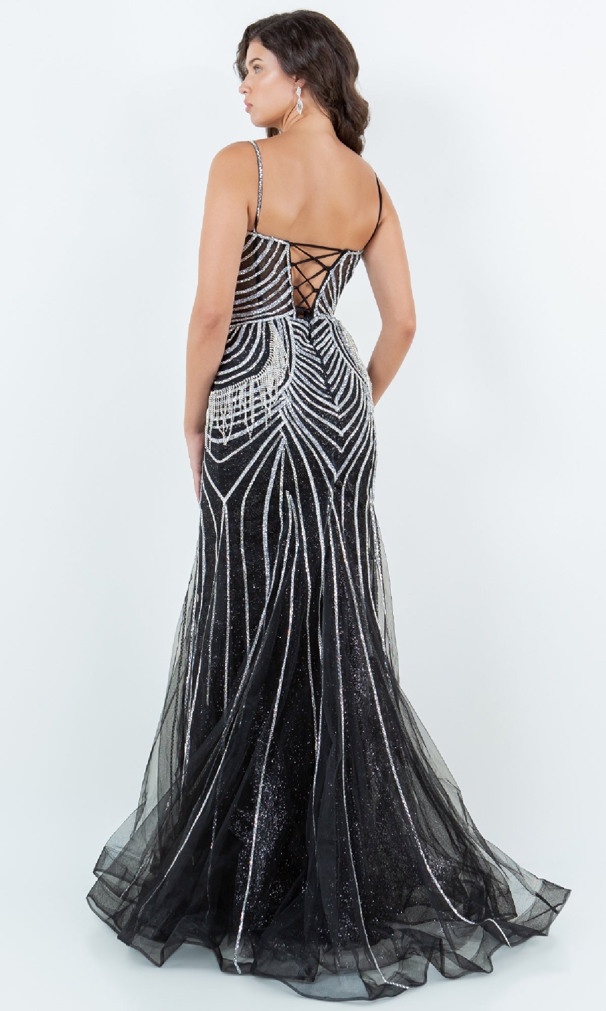 A woman in the Cinderella Couture 8192J Beaded Long Prom Dress, a black lace-up gown with spaghetti straps, geometric silver beading, and a floor-length skirt, is photographed from behind.